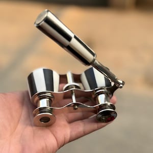 May include: Vintage opera glasses with a black and white checkered handle and matching accents. The binoculars have a silver-colored frame and lenses. A classic accessory for theater or events.
