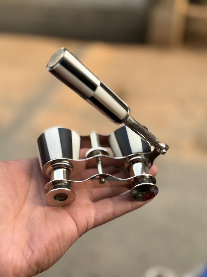 May include: Vintage opera glasses with a black and white checkered handle and matching accents. The binoculars have a silver-colored frame and lenses. A classic accessory for theater or events.