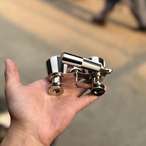 May include: A pair of opera glasses with a black and white striped design on the body and a silver-colored handle and trim. The opera glasses are held in a hand.