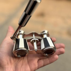 May include: A pair of vintage opera glasses with a black and white striped handle and accents. The binoculars have a silver-colored frame and lenses. The design is classic and elegant, suitable for theater or opera.