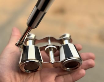 May include: A pair of vintage opera glasses with a black and white striped handle and accents. The binoculars have a silver-colored frame and lenses. The design is classic and elegant, suitable for theater or opera.