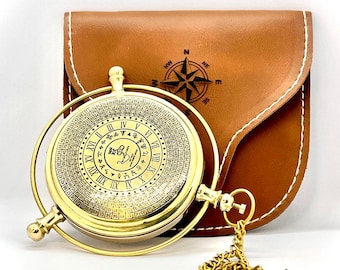 May include: A gold-colored compass with Roman numerals and intricate details, displayed with a brown leather case. The case features a compass rose design. A gold chain is attached to the compass.