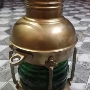 May include: A vintage brass lantern with a green glass lens. The lantern has a rounded top and base, with a handle and a small spout. The lantern is likely used for nautical or decorative purposes.