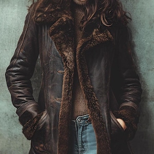 May include: A brown leather coat with a fur collar and lining. The coat has a classic design with two front pockets and button closures. The model is wearing a brown turtleneck sweater and blue jeans.