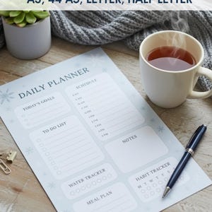 Puede incluir: Un planificador diario en PDF con el texto "DAILY PLANNER PDF A3, 44 A5, LETTER, HALF LETTER" se muestra en una superficie de madera. El planificador incluye secciones para objetivos, listas de tareas y horarios. También hay una taza de té y un bolígrafo.