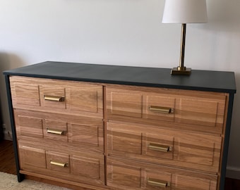 May include: A six-drawer dresser with a black top and wooden drawers. The drawers have gold-toned hardware and a wood grain pattern.