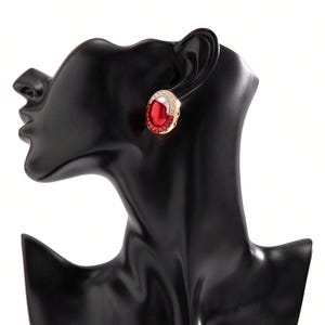 May include: A pair of gold-tone earrings with red oval-shaped stones set in a clear crystal halo.