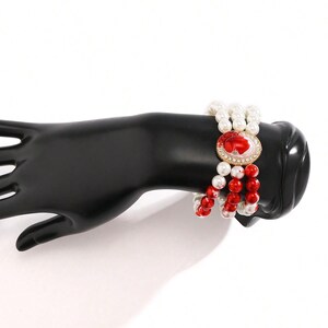 May include: A multi-strand bracelet with red and white beads and a gold-toned cameo with a red and white design.