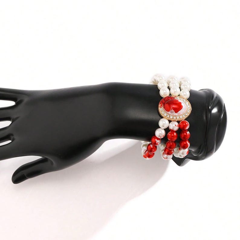 May include: A multi-strand bracelet with red and white beads and a gold-toned cameo with a red and white design.