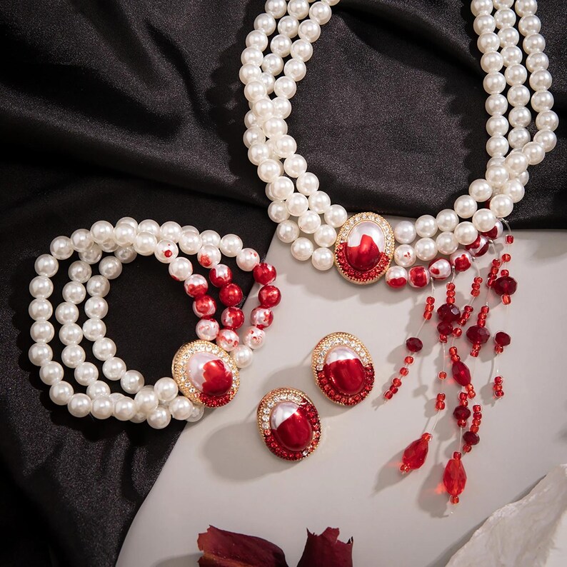May include: A pearl necklace, bracelet, and earrings set with red and white accents. The necklace has a dangling charm with red beads.