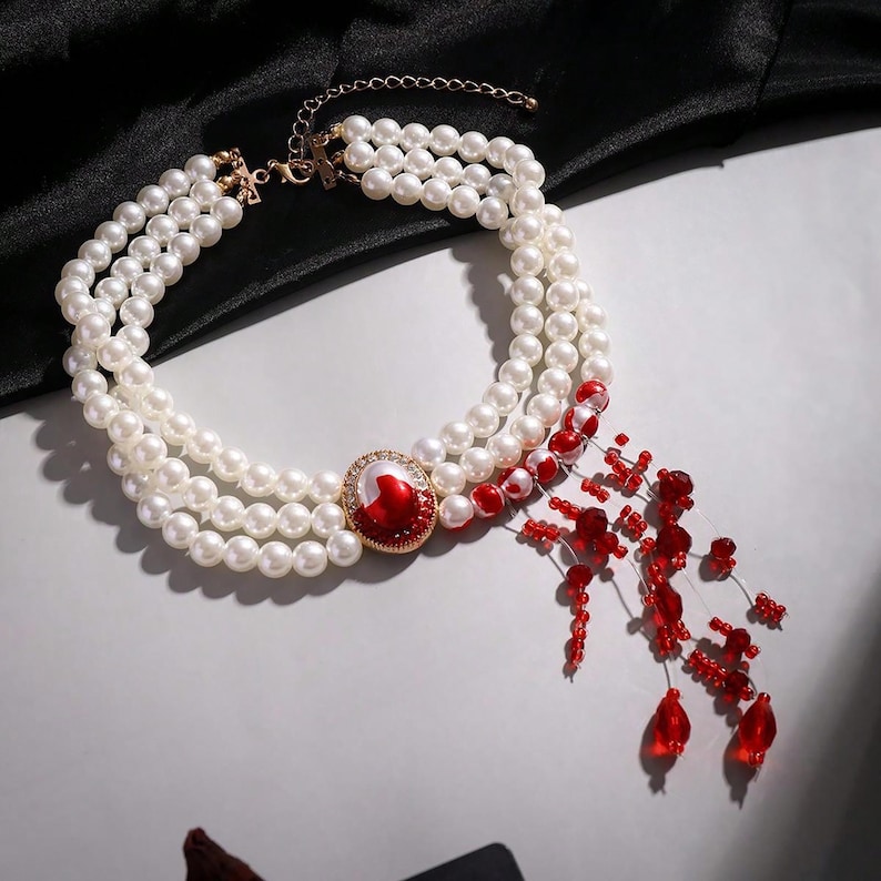 May include: A three-strand pearl choker necklace with a red and gold centerpiece and a dangling strand of red beads.