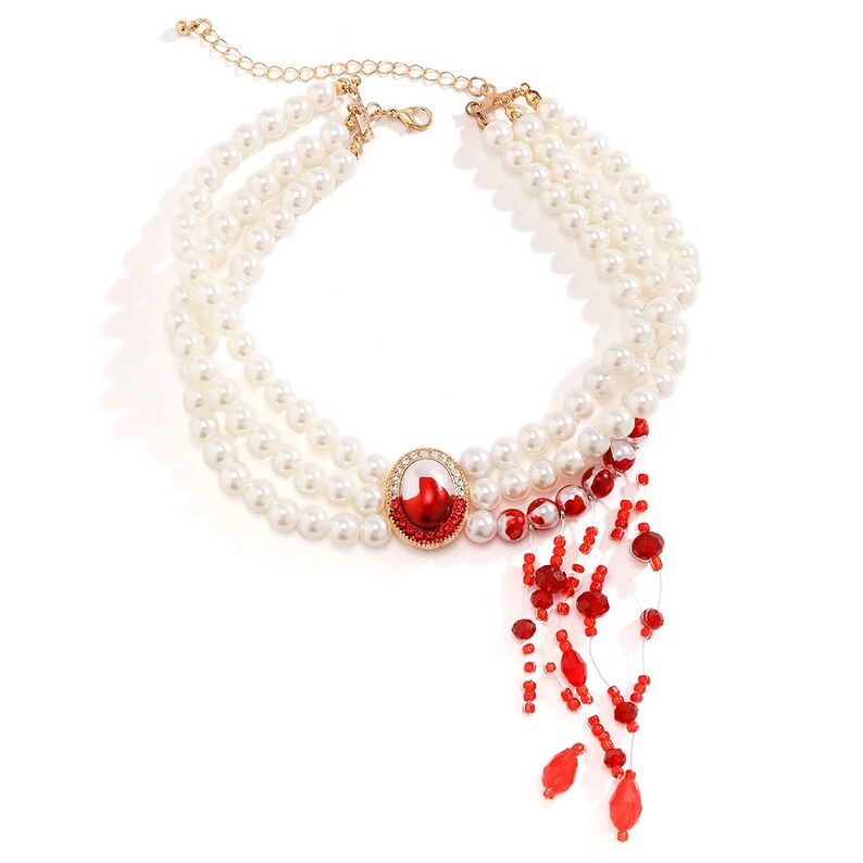 May include: A white pearl necklace with a red and white jeweled pendant and a red beaded fringe.