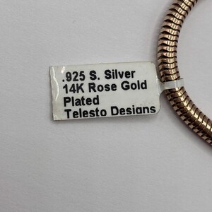 May include: A close-up of a rose gold-plated chain with a tag that reads ".925 S. Silver 14K Rose Gold Plated Telesto Desians."