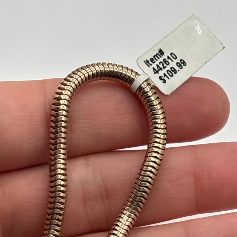 May include: A gold-colored, snake chain necklace is displayed against a light background. The necklace is made of small, interlocking metal segments. A white tag with the text "Item# 442610" is attached to the necklace.