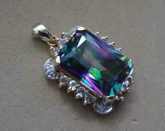 May include: A gold pendant featuring a large, rectangular, iridescent gemstone with shades of green, purple, and blue. The gemstone is surrounded by smaller, clear gemstones. The pendant has a gold bail.