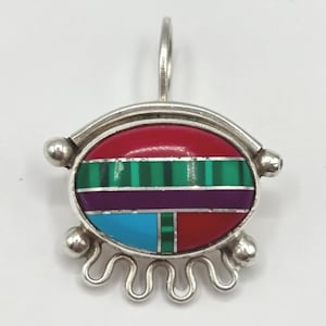 May include: A silver pendant with an oval, inlaid design. The design features red, green, purple, and blue sections. The pendant has a loop at the top and decorative silver elements at the bottom.