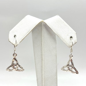 May include: A pair of silver-toned Celtic knot earrings. Each earring features a triangular knot design suspended from a hook. The earrings are displayed on white earring display cards against a light background.