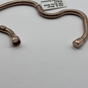 May include: Rose gold-plated bracelet with a flexible, textured design. The bracelet is made of .925 silver and 14K rose gold. The bracelet is shown on a white surface.