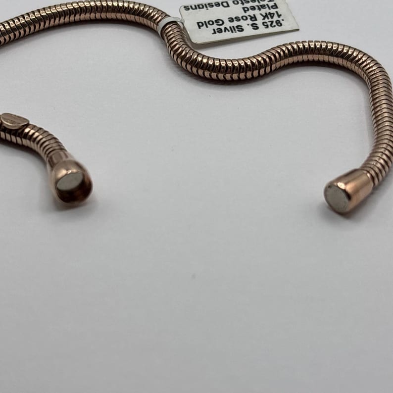 May include: Rose gold-plated bracelet with a flexible, textured design. The bracelet is made of .925 silver and 14K rose gold. The bracelet is shown on a white surface.