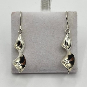 May include: A pair of silver-colored spiral drop earrings. The earrings have a polished, reflective surface and a hook closure. The design features a flowing, twisted shape, creating a modern and elegant look. The earrings are displayed on a gray velvet surface.