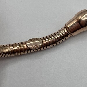 May include: Close-up of a rose gold necklace with a snake chain design. The clasp is stamped with "ITALY" and "925". The necklace has a polished finish and is set against a neutral background.