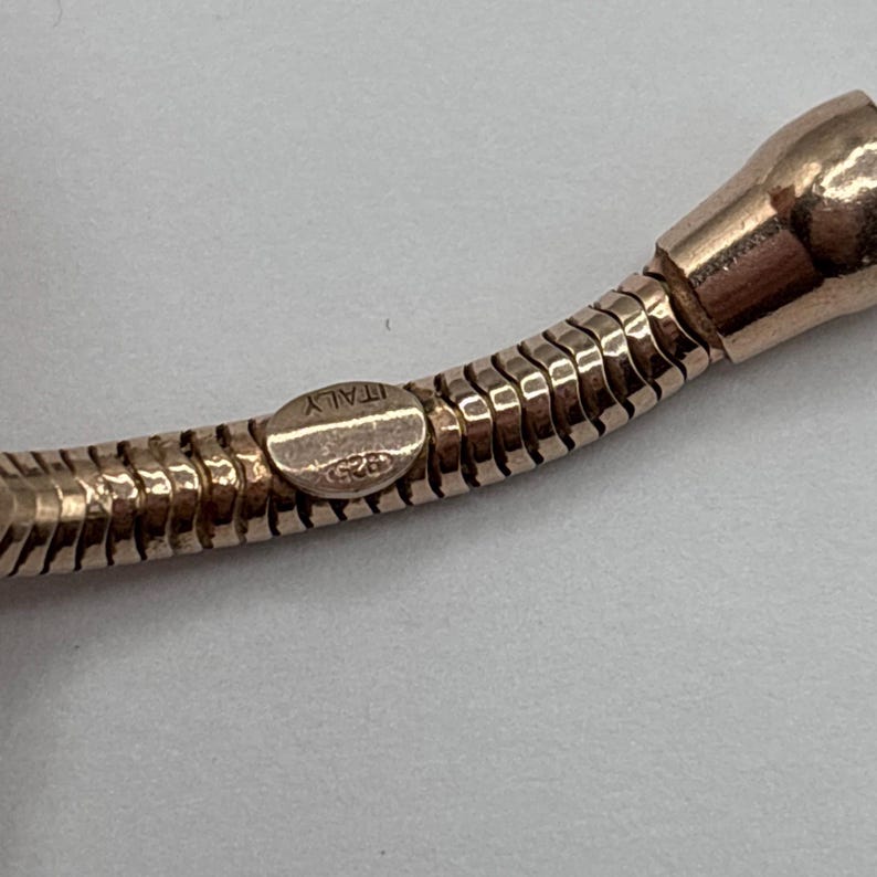 May include: Close-up of a rose gold necklace with a snake chain design. The clasp is stamped with "ITALY" and "925". The necklace has a polished finish and is set against a neutral background.