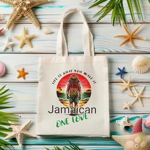 May include: White tote bag with a graphic featuring a person with dreadlocks, the words "Jamaican One Love", and the phrase "Life is what you make it". The bag is surrounded by starfish and seashells.