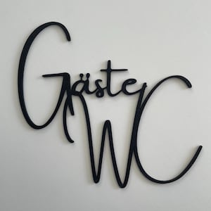 Könnte beinhalten: Schwarze Wandkunst in Schreibschrift mit der Aufschrift "Gäste WC" auf weißem Hintergrund. Die Buchstaben sind in einer fließenden Schrift verbunden, wobei "Gäste" über "WC" steht. Ein dekoratives Element für ein Badezimmer oder einen Gästebereich.
