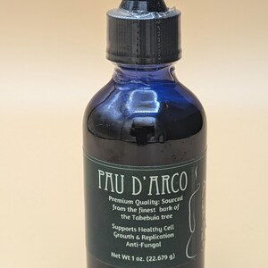 May include: A dark blue glass bottle with a black dropper top. The bottle is labeled "Pau D'Arco" and contains a dark liquid. The label also states "Premium Quality: Sourced from the finest bark of the Tabebuia tree" and "Supports Healthy Cell Growth & Replication Anti-Fungal". The bottle contains 1 ounce (22.679 grams) of liquid.