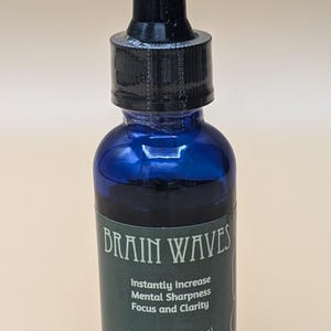 May include: A blue glass bottle with a black dropper top. The bottle has a green label that reads "BRAIN WAVES" and lists the benefits of the product: "Instantly Increase Mental Sharpness Focus and Clarity". The label also states "Net Wt 1 oz. (22.679 g)".