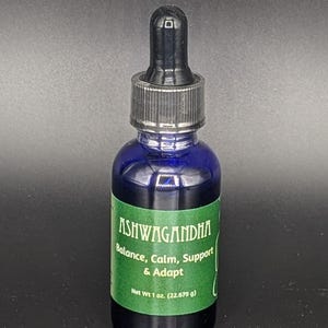 May include: A blue glass bottle with a black dropper top. The bottle is labeled "Ashwagandha" and contains a liquid. The label also says "Balance, Calm, Support & Adapt" and "Net Wt 1 oz. (22.679 g)".