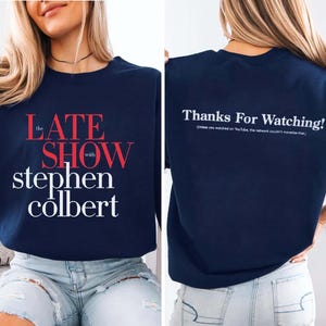 May include: Navy blue sweatshirt with the text "The Late Show with Stephen Colbert" in red and white. The back of the sweatshirt has the text "Thanks For Watching!" in white. A casual, long-sleeved top.