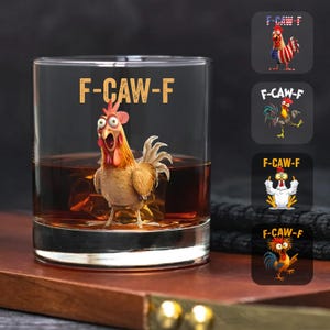 May include: A clear whiskey glass with the text "F-CAW-F" and a cartoon rooster illustration. The glass is filled with amber liquid and sits on a wooden surface. Additional rooster designs are displayed on the right.