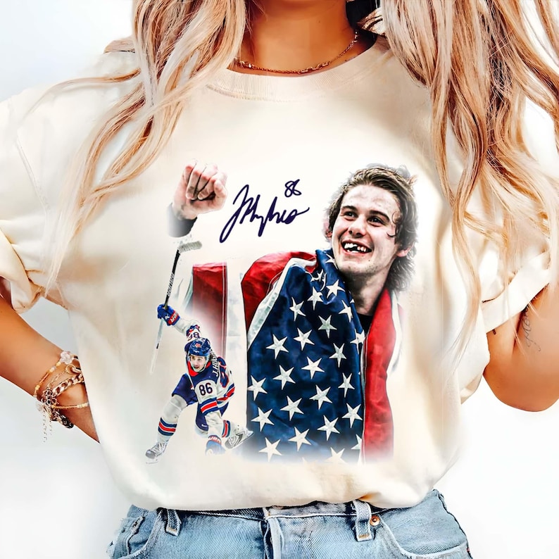 May include: Cream-colored t-shirt featuring a graphic of a hockey player with an American flag. The image includes a signature and the number 86. The player is shown celebrating with a flag draped over his shoulders.