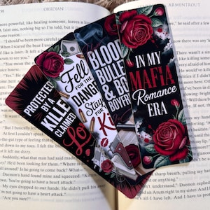 May include: A stack of four decorative bookmarks with romantic themes. Each bookmark features text, roses, and other graphics. The bookmarks are on top of an open book.