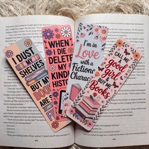 May include: Four colorful bookmarks with floral designs and text. The bookmarks read: "I DUST MY SHELVES BUT MY BOOKS ARE FINE", "WHEN I DIE DELETE MY KIND HIST", "I'm in Love with a Fiction Character", and "CALL ME A good girl & BUY ME Books".