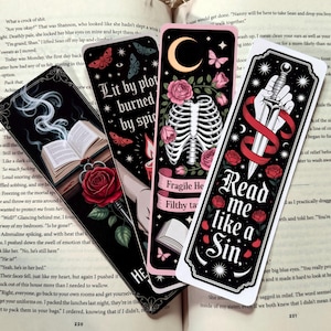 May include: Four gothic-style bookmarks with dark backgrounds. One features an open book with smoke, a rose, and the text "Lit by plot burned by spig." Another shows a rib cage, roses, and the text "Fragile Heart, Filthy Taste." The third has a hand holding a dagger, roses, and the text "Read me like a Sin."