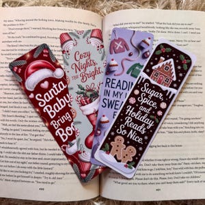 May include: Four festive bookmarks with holiday themes are displayed open on a book. The bookmarks feature Christmas designs, including Santa, gingerbread men, and text like "Cozy Nights" and "Sugar, Spice, and Holiday Reads So Nice."