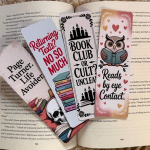 May include: Four colorful bookmarks with humorous quotes and illustrations are displayed on an open book. The bookmarks feature phrases like "Returning Texts? No So Much" and "Book Club or Cult? Unclear."