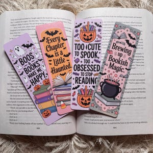 May include: Four Halloween-themed bookmarks with spooky phrases and illustrations. The bookmarks feature ghosts, bats, pumpkins, and candy corn. Text includes "Boos & Books Make Me Happy," "Every Chapter is a Little Haunted," "Too Cute to Spook, Too Obsessed to Stop Reading," and "Brewing Up Bookish Magic."