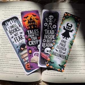 May include: Four Halloween-themed bookmarks with spooky designs and text. One reads "I SMELL BOOKS, NOT FEAR," another "TALES FROM THE TBR CRYPT," a third "DEAD INSIDE BUT READING," and the last "ONE PAGE CLOSER TO HALLOWEEN."