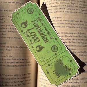 May include: Green bookmark with a ticket design. The text on the bookmark reads "Lifetime member of Forbidden Love Book Club" and "One Night Only". The bookmark has a scalloped edge and flame and circle graphics.