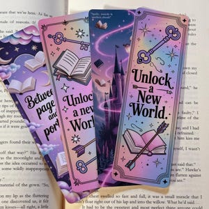 May include: Four fantasy-themed bookmarks with pastel gradients. Each bookmark features illustrations of books, keys, arrows, and castles. Text on the bookmarks reads "Between page and portal" and "Unlock a New World."