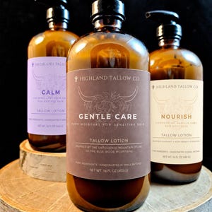 Op de afbeelding: Drie amberkleurige glazen flessen met zwarte pompdoseerders, elk met 453 g talklotion. De etiketten bevatten een illustratie van een Schotse hooglander en de tekst Highland Tallow Co., met de namen Calm, Gentle Care en Nourish.
