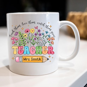 May include: White ceramic mug featuring a colourful floral design and the word "TEACHER" in bubble letters. A yellow pencil graphic with "Mrs Smith" is below the word. The mug has the text "Teach them, love them, watch them grow."