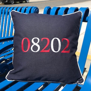 Puede incluir: Una almohada azul marino con ribete blanco y el número "08202" bordado en rojo y blanco.