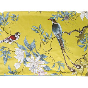 May include: A decorative pillow with a vibrant yellow background featuring a detailed print of birds, flowers, and foliage. The design includes a long-tailed bird perched on a branch, with white and blue accents.
