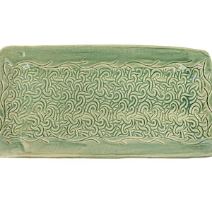 May include: A rectangular ceramic tray in a sage green glaze featuring a central panel with an intricate, repeating embossed swirl pattern and a smooth, plain border framed by a thin, carved line that follows the edge of the tray.