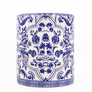 May include: A cylindrical ceramic vessel featuring a white base with a symmetrical blue floral pattern. The design includes intricate line-drawn roses and scrolling foliage, finished with a decorative geometric border along the bottom edge.