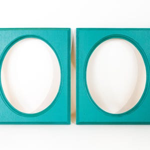 May include: Two rectangular picture frames with oval-shaped center openings. The frames are painted in a solid, vibrant teal color and feature a smooth, flat surface with beveled edges surrounding the central oval cutouts for displaying photos.